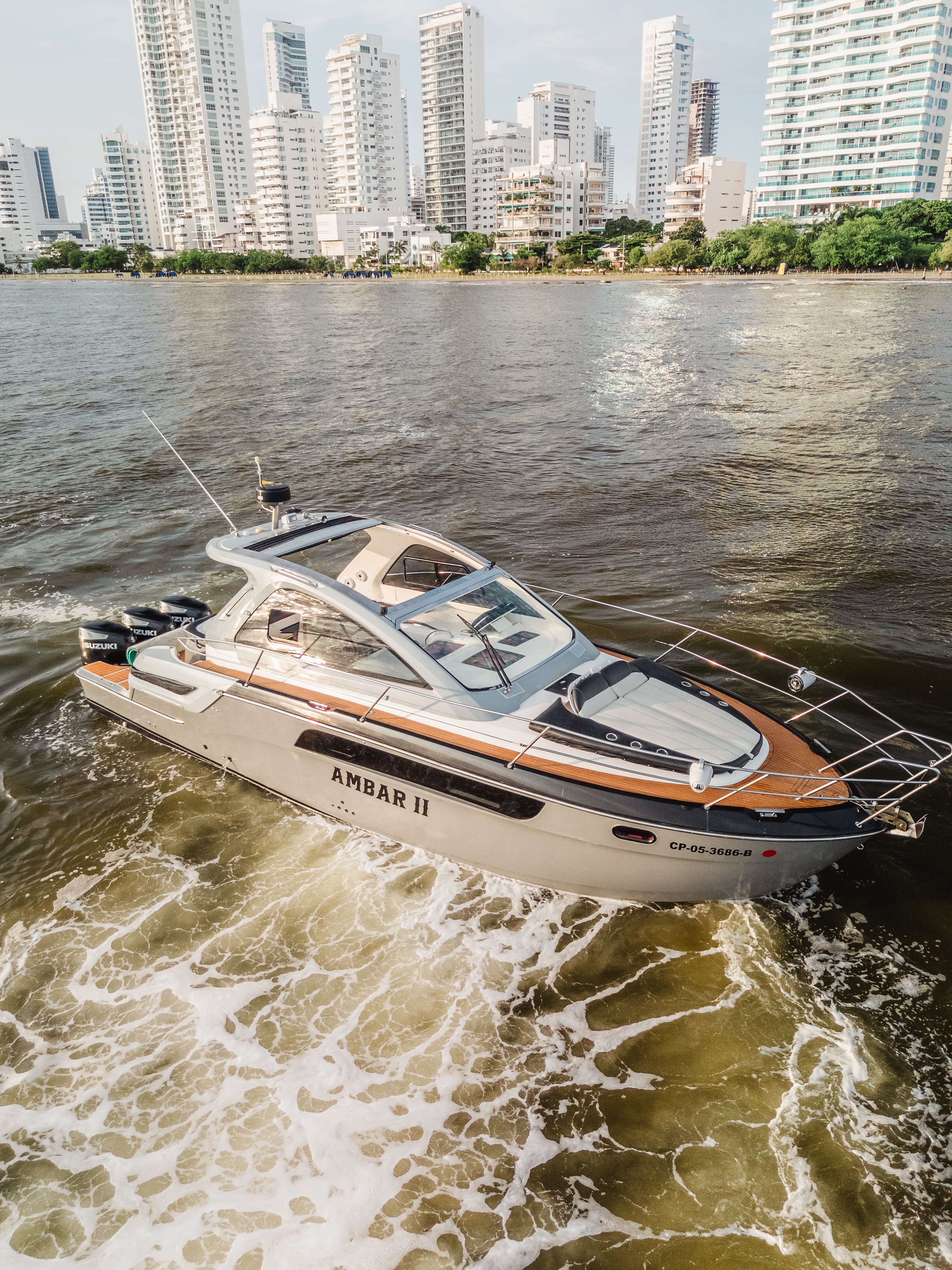 AMBAR II white motor yacht with teak decks cruising past the Cartagena high-rise skyline, its name visible on the hull