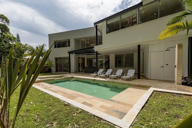 Daytime view of Villa Bali's modern white and graphite facade with a swimming pool, sun loungers and a lawn surrounded by trees