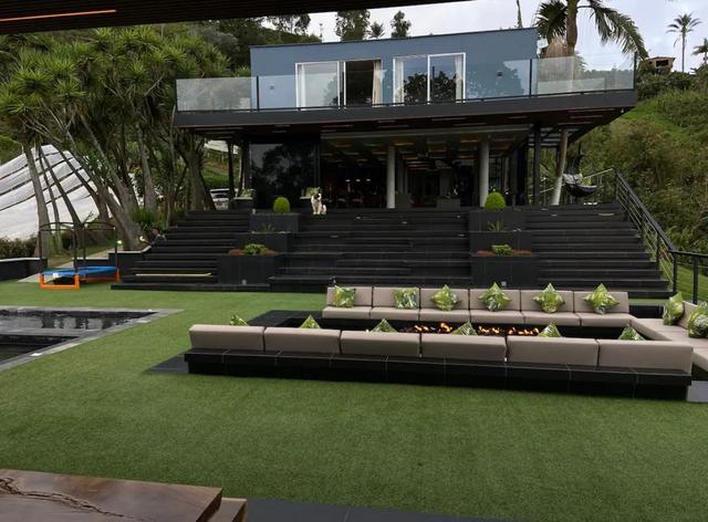 Daytime view of a two-storey lake house with a glass balcony, broad black steps and a sunken firepit lounge.