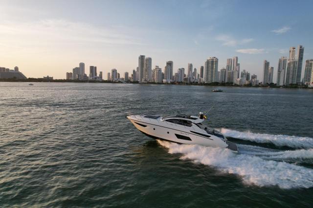 White Azimut 48 hardtop yacht cruising at speed with a white wake, the Cartagena high-rise skyline behind