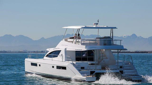 White twin-hulled powercat underway, viewed from the aft quarter with its covered flybridge and wake visible.