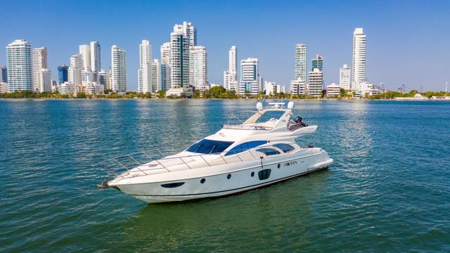 White Azimut flybridge yacht at anchor on turquoise water with the Cartagena high-rise skyline behind