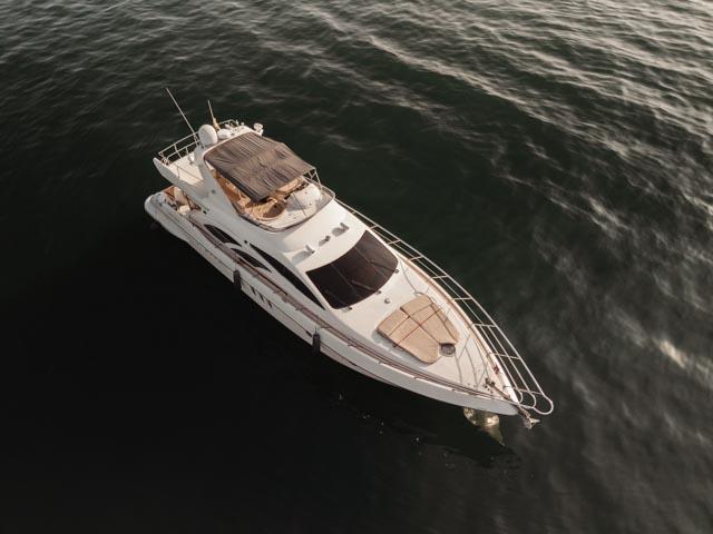 Aerial view of the full white Azimut flybridge yacht with a tan canopy and bow sunpads on dark open water