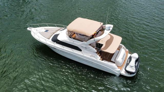 Drone view of the white Sea Ray flybridge yacht with tan canopies and a jet ski on its swim platform on green water
