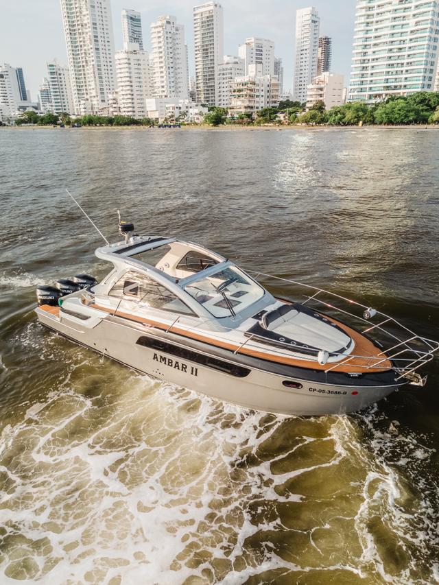 AMBAR II white motor yacht with teak decks cruising past the Cartagena high-rise skyline, its name visible on the hull