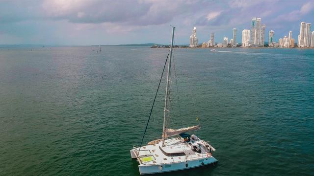 Aerial view of a white sailing catamaran with twin hulls and mast against the Cartagena waterfront skyline