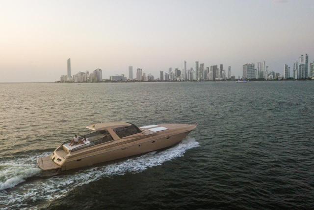 Long, low champagne-coloured motor yacht cruising across the bay with the Cartagena skyline behind at dusk