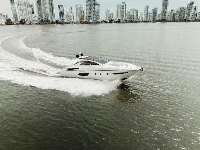 White hardtop yacht cruising at speed in a curving wake, with a row of Cartagena high-rises behind