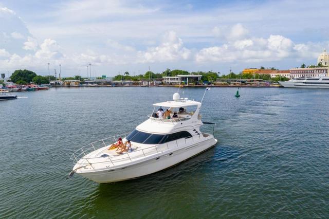 White Sea Ray flybridge yacht underway in Cartagena harbor with guests on the bow sunpad and the city waterfront behind