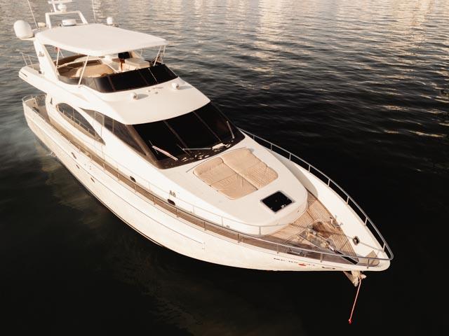 Front three-quarter aerial view of the white Sea Land yacht at golden hour, showing the bow sunpad and flybridge