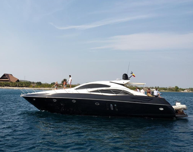 Side profile of the black-hulled Sunseeker Predator underway with guests on deck and a tender at the stern