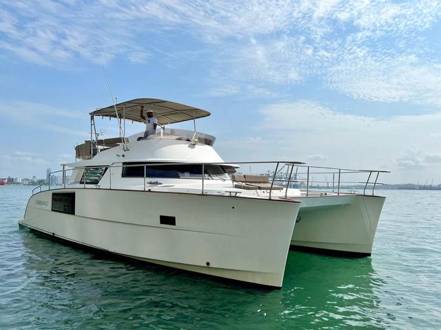 White twin-hulled powercat on calm water with CUMBERLAND branding and a shaded flybridge