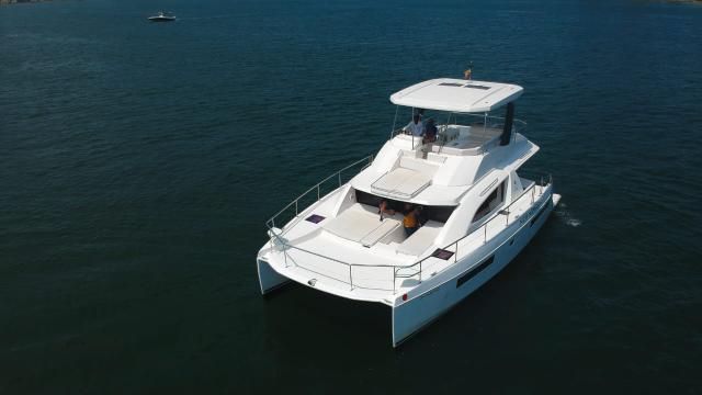 Aerial bow-quarter view of New Horizon, a white twin-hulled powercat with foredeck cushions and a covered flybridge.