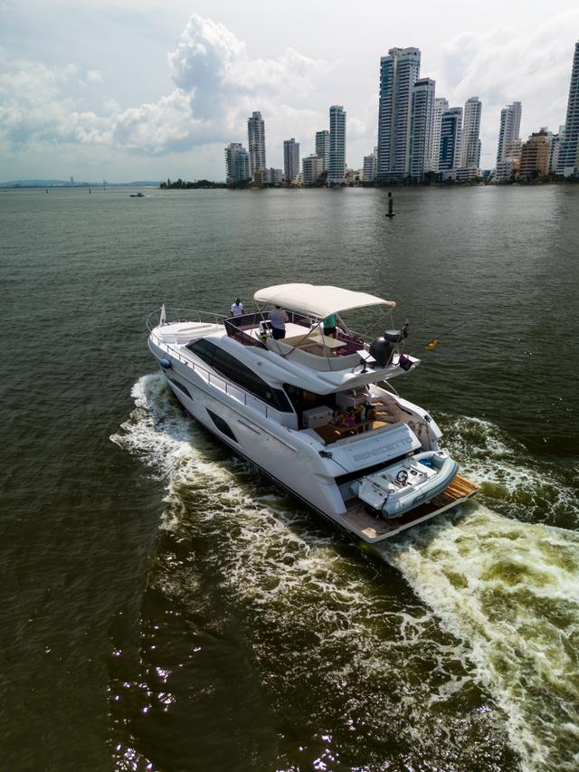 Aerial view of the white flybridge yacht cruising and leaving a long wake, with the Cartagena skyline across the bay