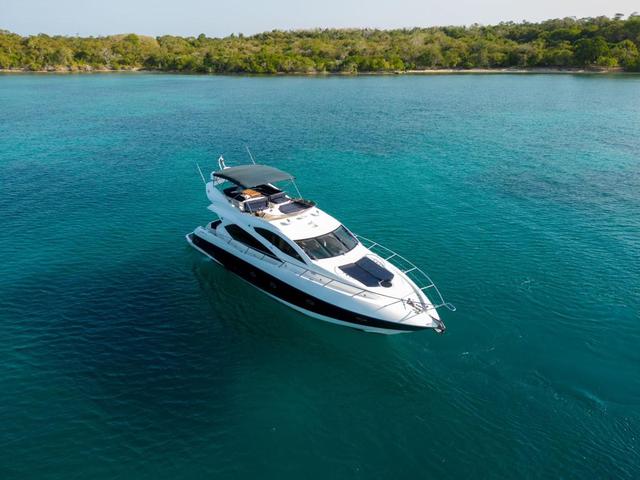 Aerial view of the white Sunseeker flybridge yacht at anchor on turquoise water with a wooded shoreline behind