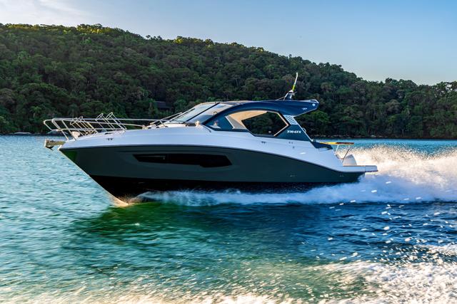 White and dark grey hardtop boat cruising at speed with a white wake past a forested hillside