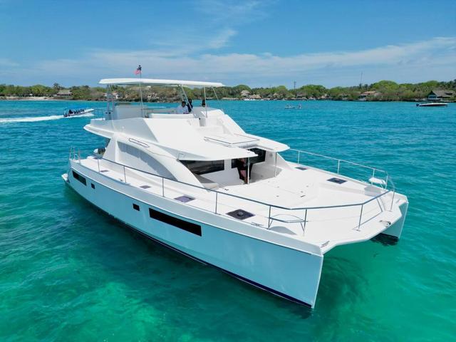 Elevated bow-quarter view of a white twin-hulled powercat with a broad foredeck and covered flybridge on turquoise water.