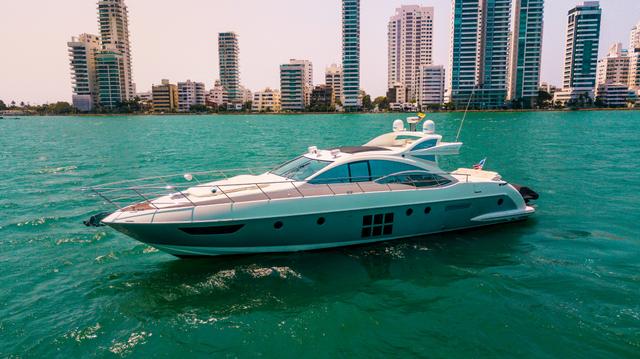 White and grey Azimut hardtop yacht at anchor on turquoise water in front of Cartagena's high-rise skyline